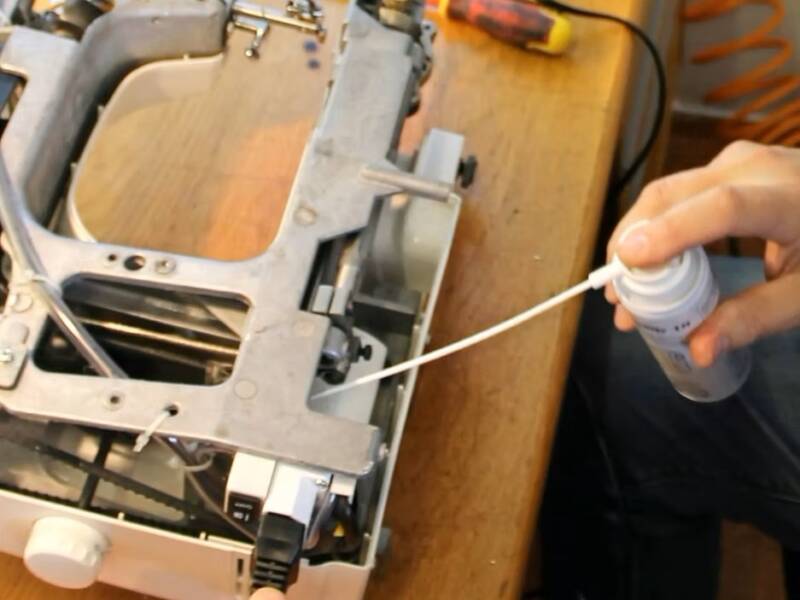 Cleaning a sewing machine with a can of compressed air.