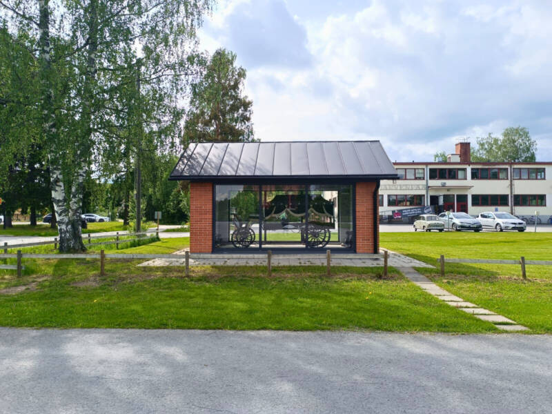 The hearse is displayed in a glass case, with the Iisakki Järvenpää Knife Factory in the background.